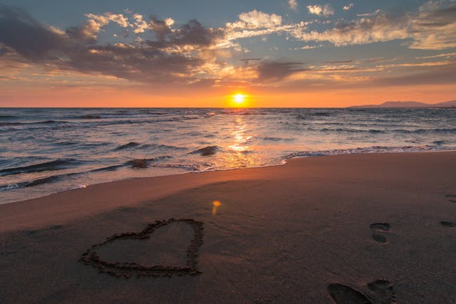 un corazón dibujado en la arena a la orilla del mar en el atardecer.